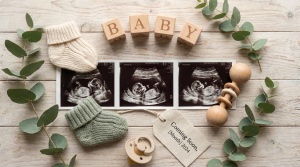 Beautiful pregnancy announcement flat-lay: ultrasound image surrounded by baby shoes, wooden letter blocks spelling 'BABY', e
